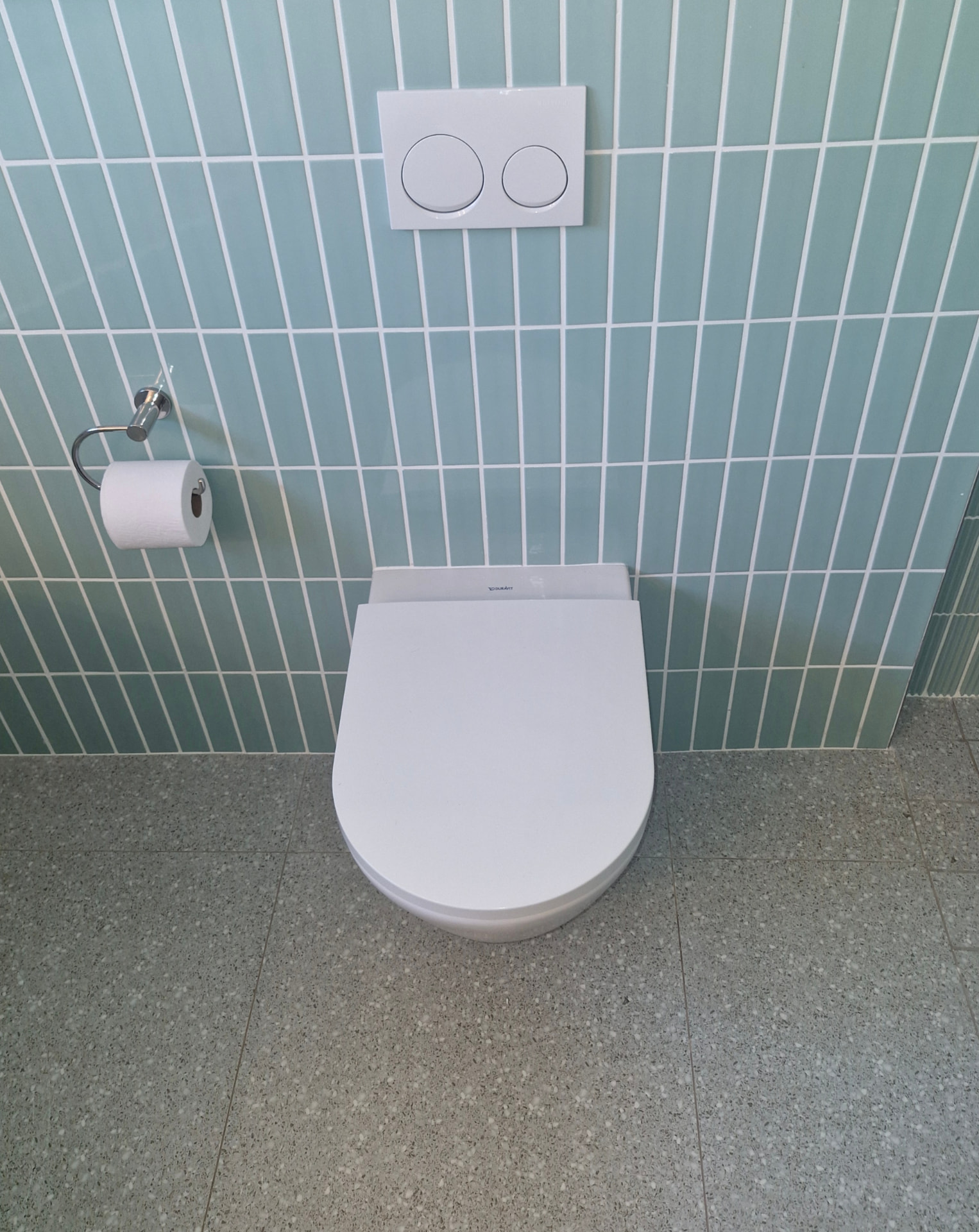 Wall-mounted toilet against pale teal vertical tiles