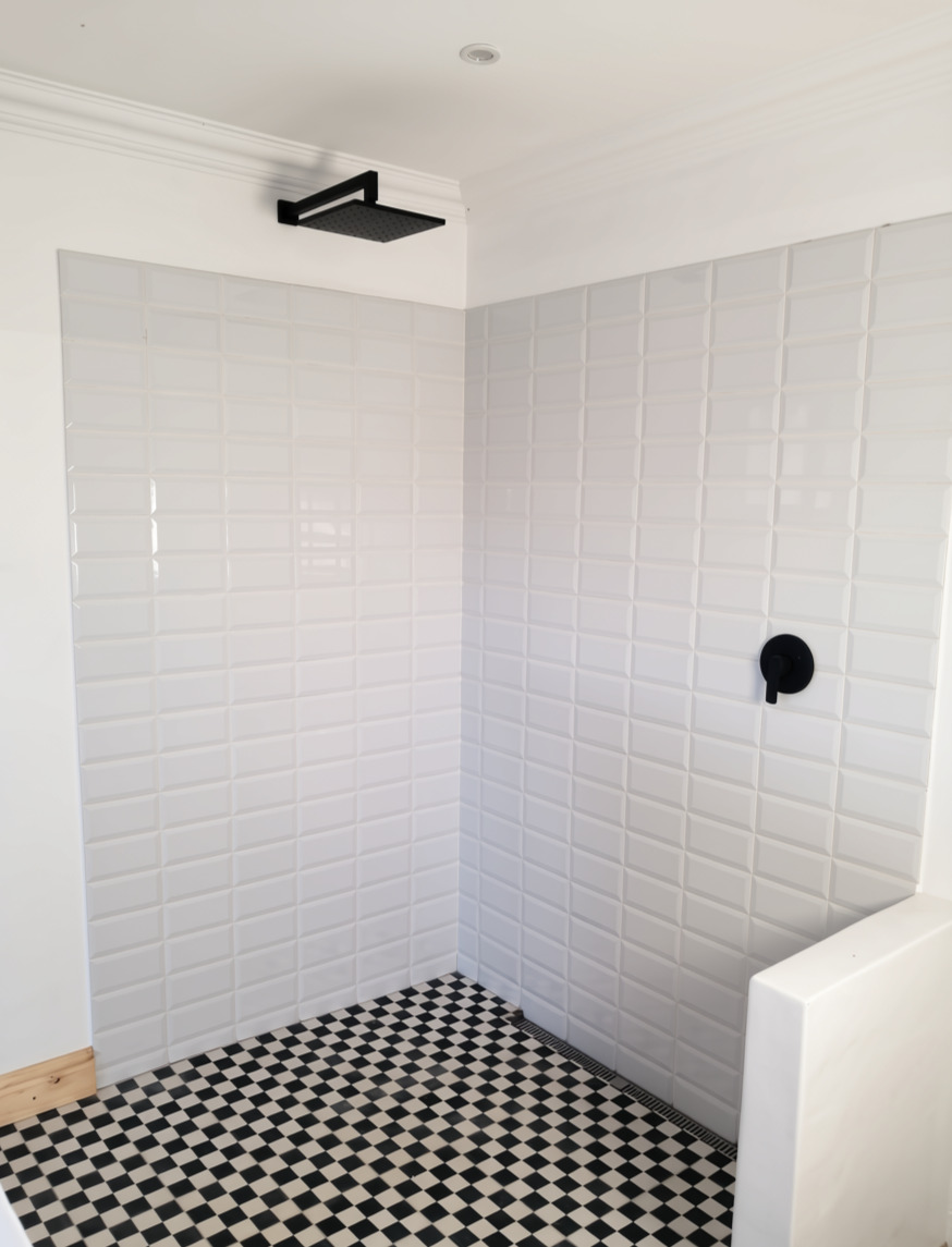 White tiled walk-in shower with black fittings and a checkerboard floor